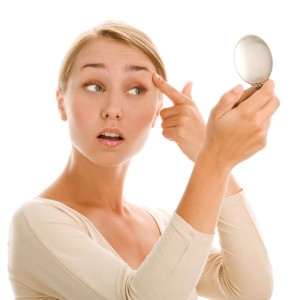 A young woman looking in a compact mirror and pulling up on here eyelids on a white background
