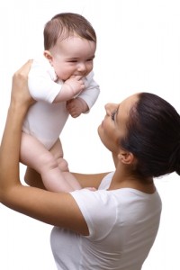 A brunette mother in a white t-shirt holding up here baby in a white onesie on a white background